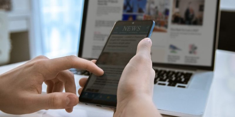 person looking at news on computer and phone