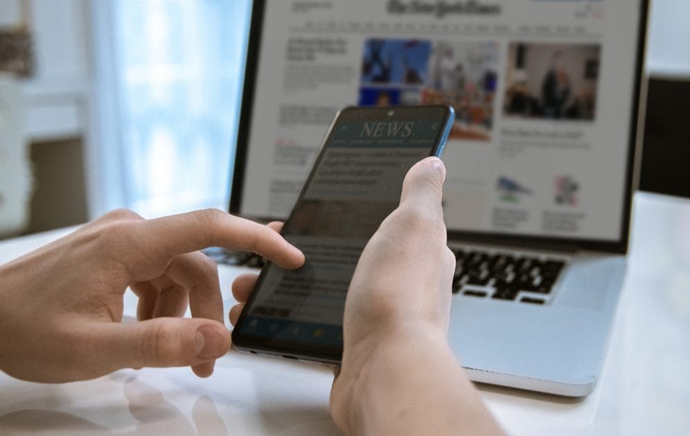 person looking at news on computer and phone